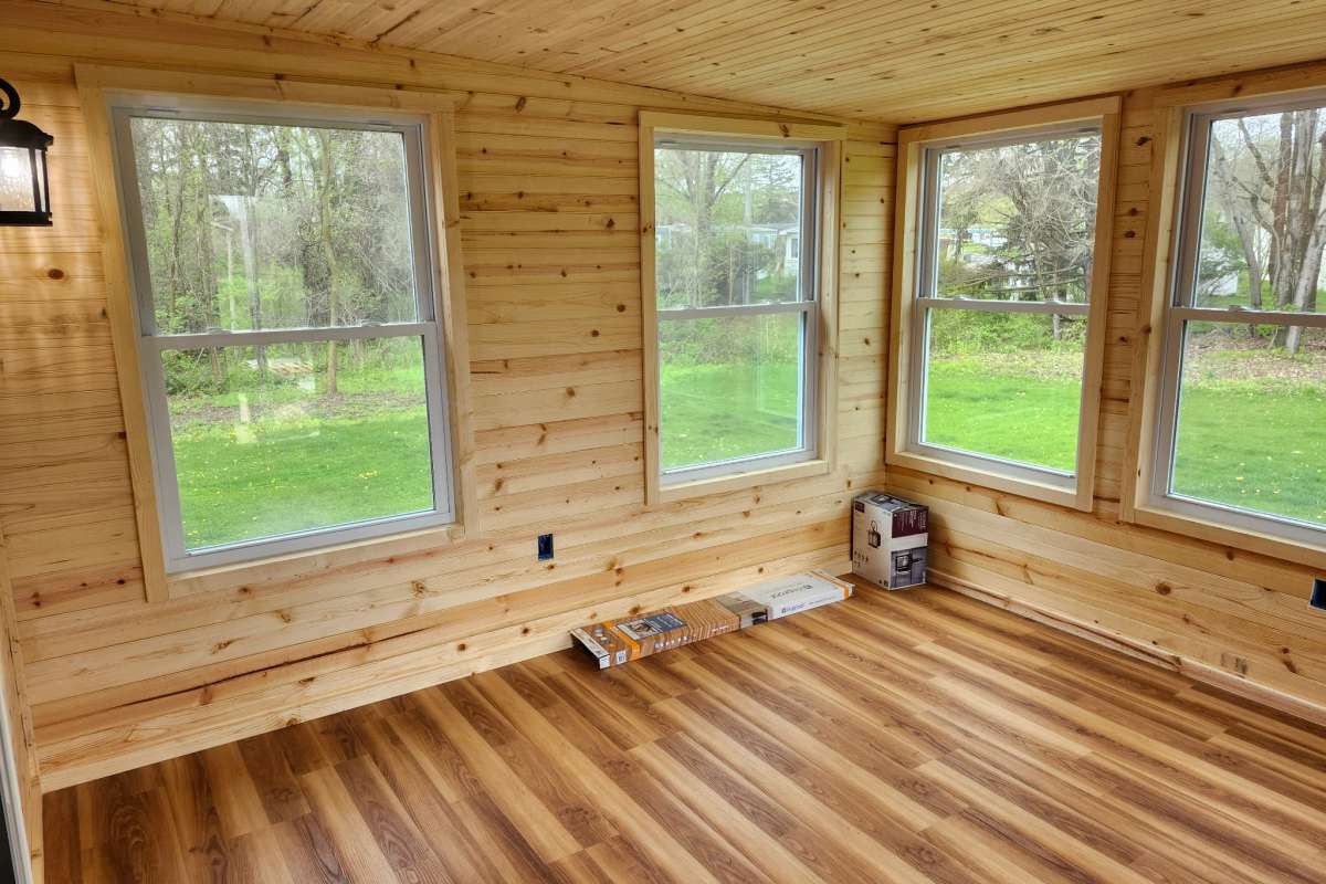 New room with pine plank walls and ceiling, large windows, and wood-look flooring.