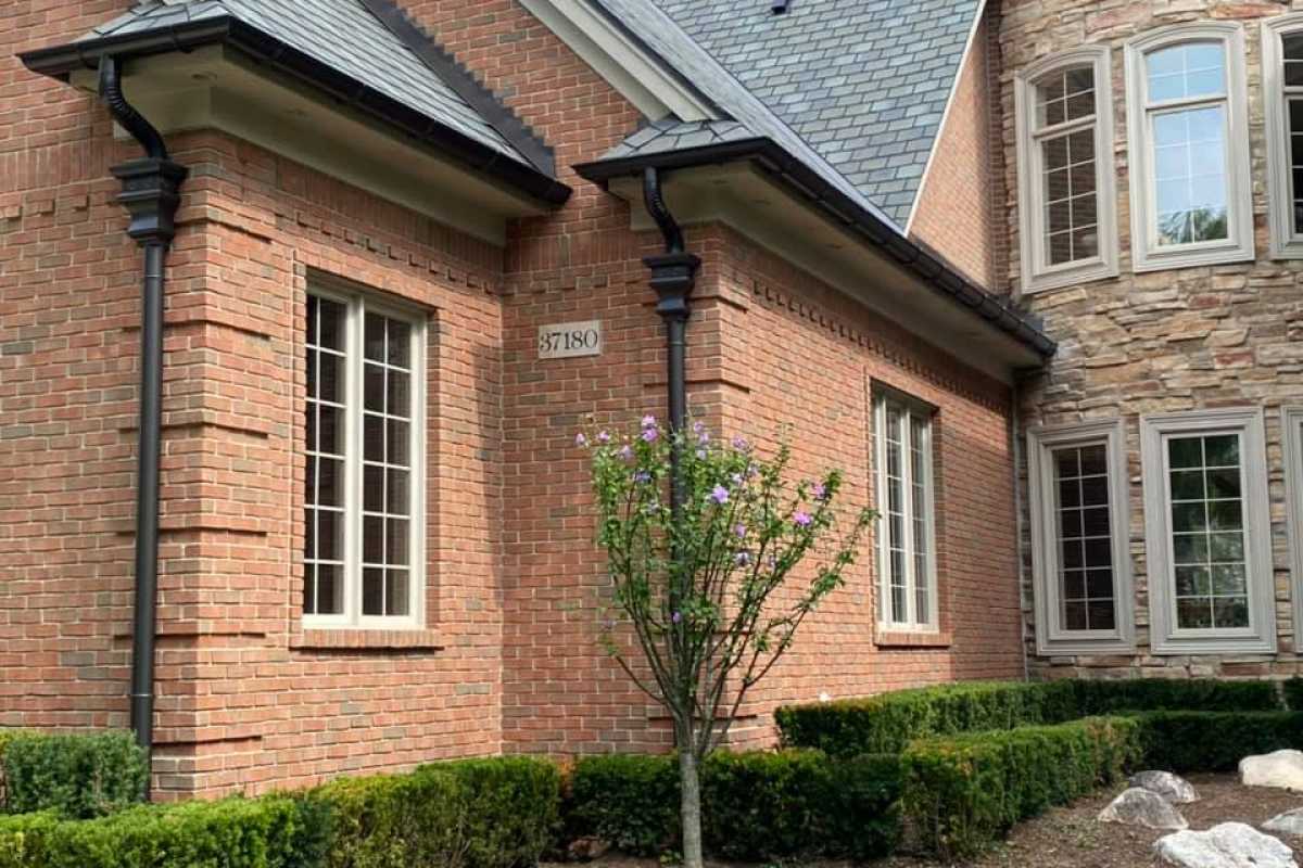 Black residential seamless gutters installed on brick house by Michigan Exterior Pros.